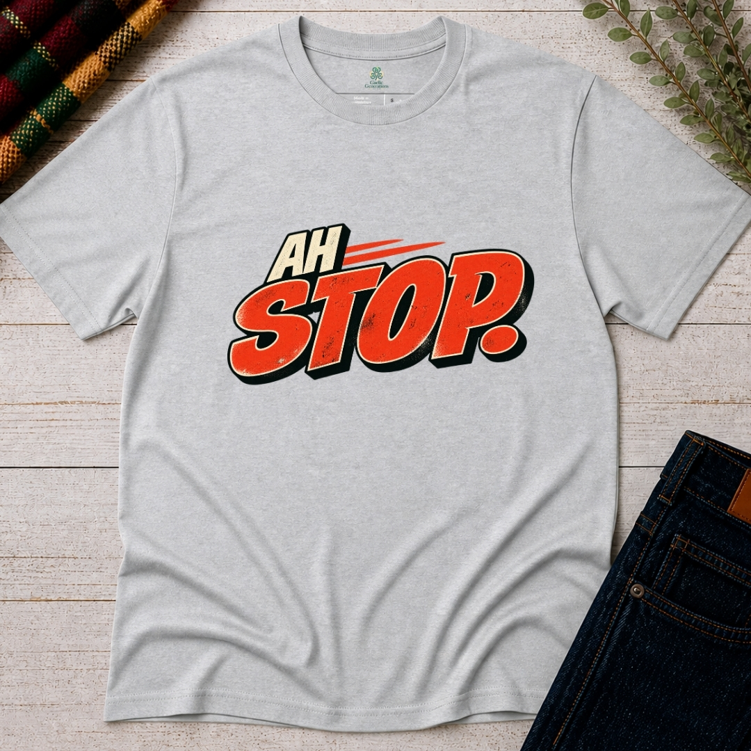 Ash grey Ah Stop Irish saying T-shirt with bold distressed red-orange lettering and cream accents, displayed flat on rustic wood