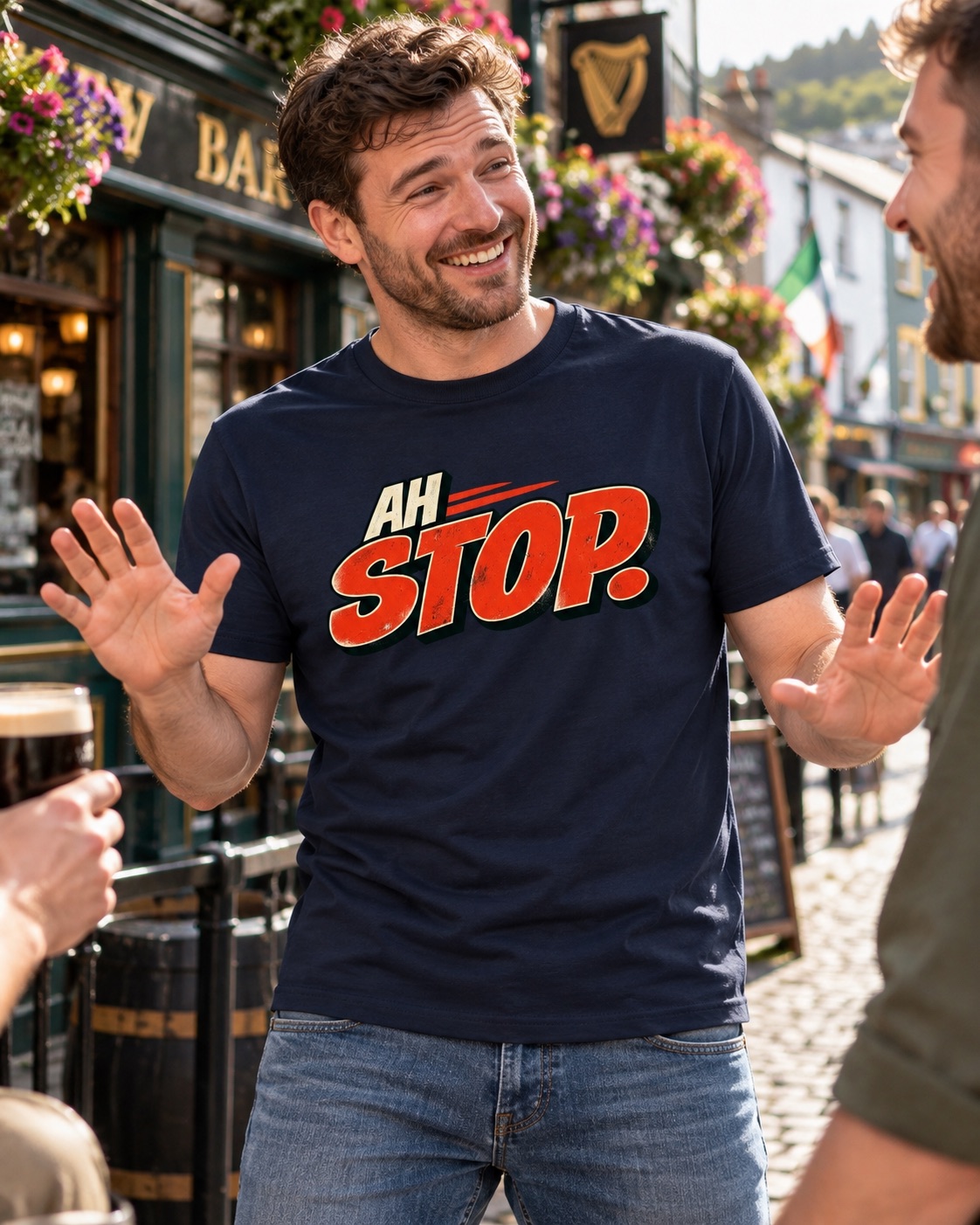 Man wearing navy Ah Stop Irish saying T-shirt, smiling and gesturing with both hands while talking outside a pub