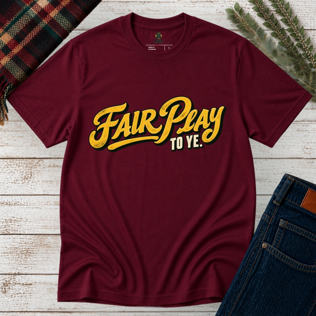 Maroon Fair Play To Ye T-shirt laid flat on rustic wood, featuring bold golden-yellow vintage script and cream Irish slang lettering