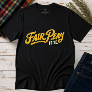 Black Fair Play To Ye Irish saying T-shirt with vintage golden-yellow script and cream lettering, displayed flat on a rustic wooden background