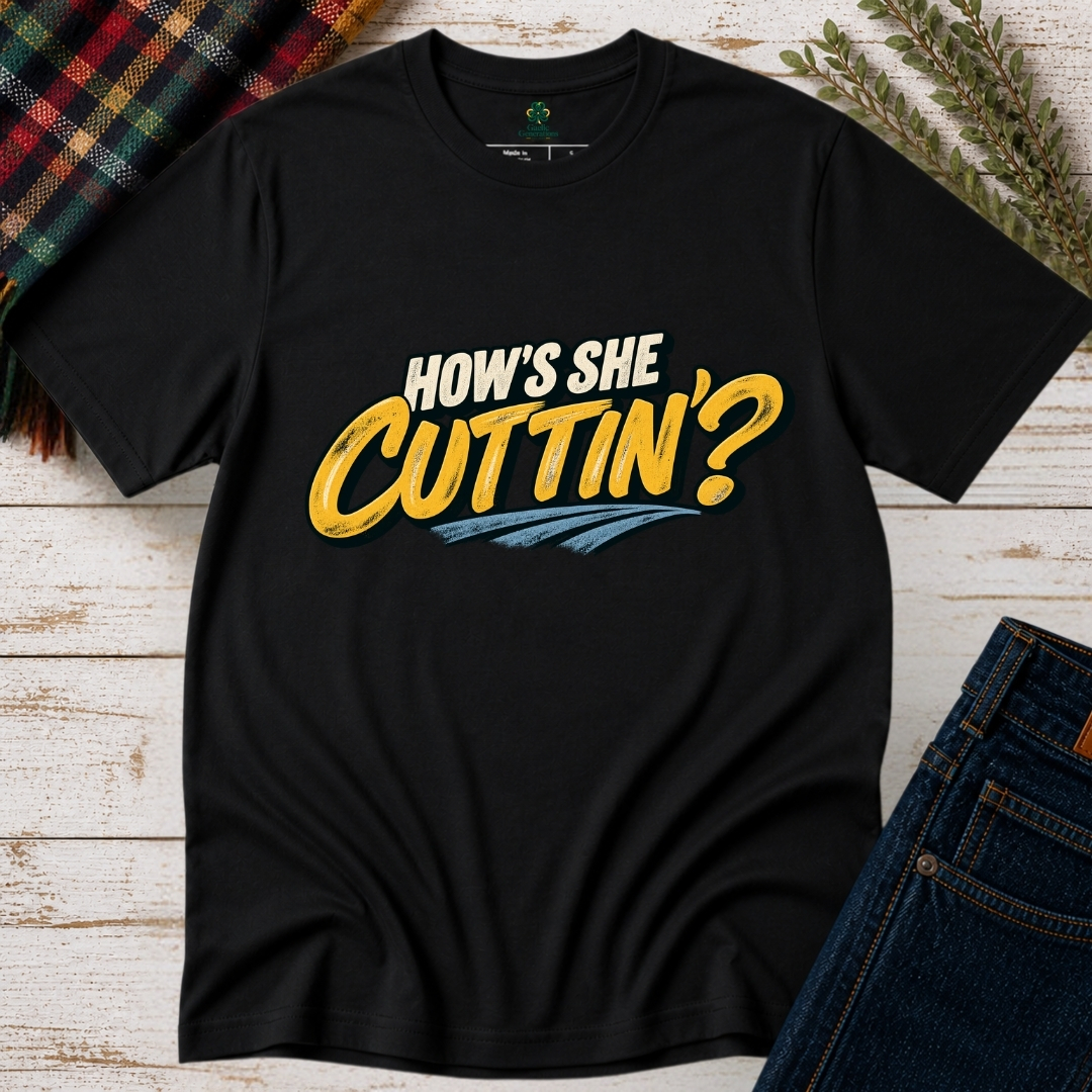 Black How's She Cuttin' Irish saying T-shirt with cream lettering, vintage yellow script and blue accents, displayed flat on rustic wood