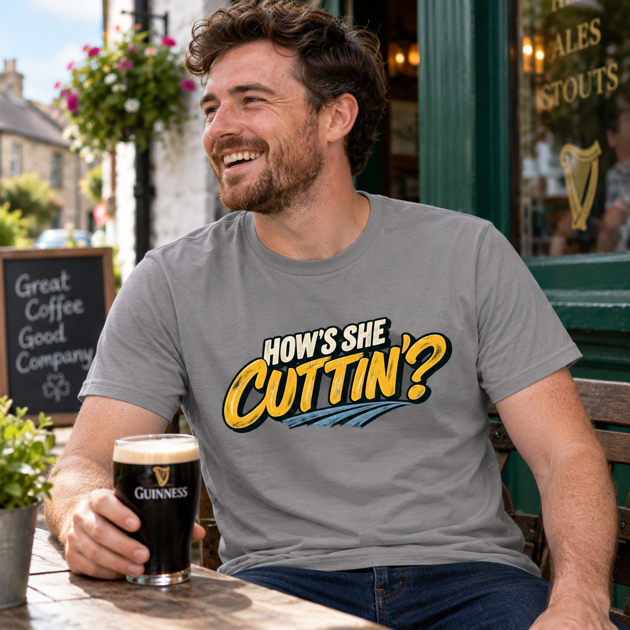 Man wearing charcoal grey How's She Cuttin' Irish saying T-shirt, smiling with a pint outside a village pub