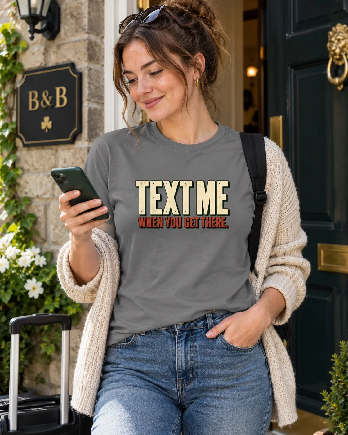 Woman wearing a charcoal Text Me When You Get There T-shirt while checking her phone outside an Irish B&B