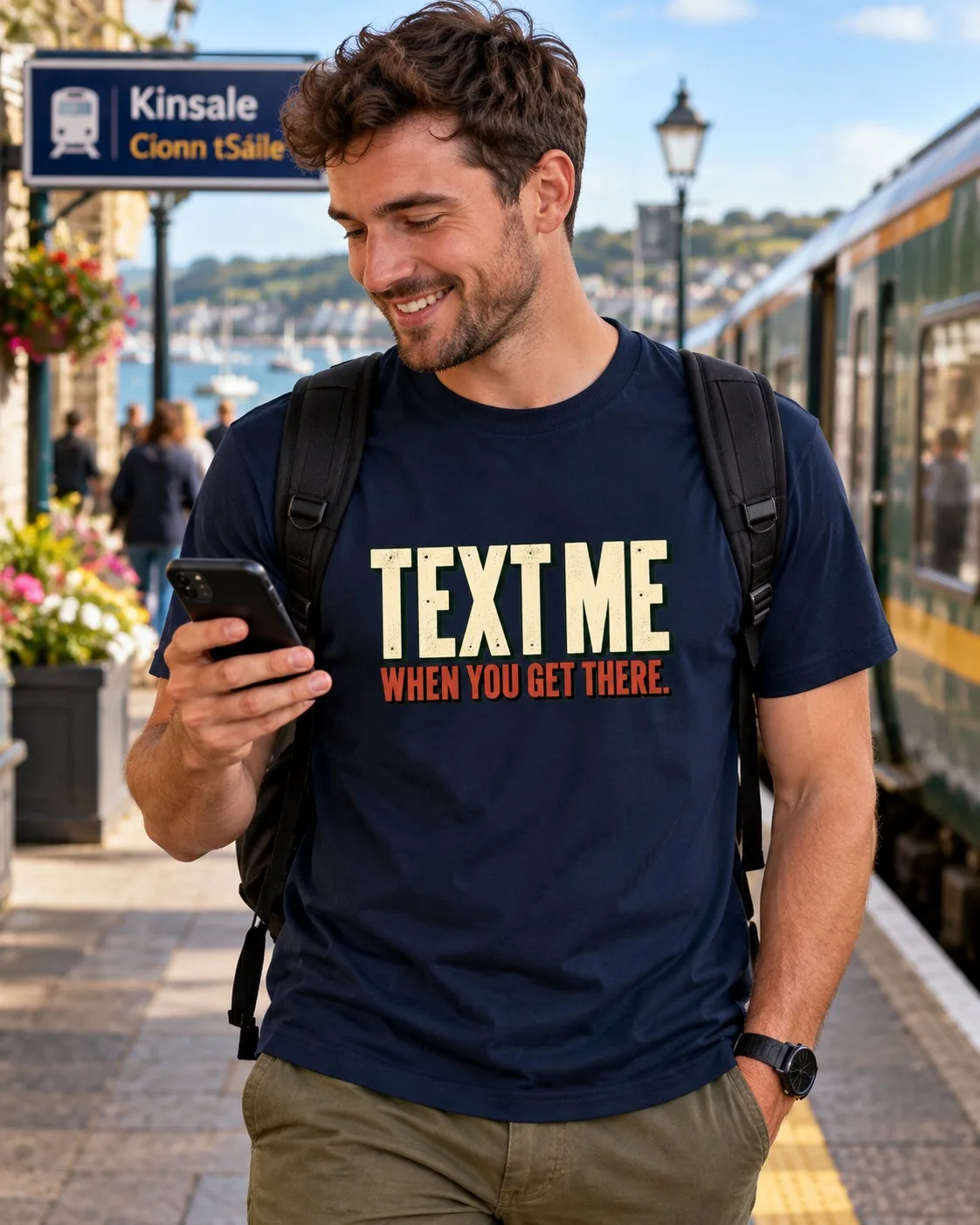 Man wearing a navy Text Me When You Get There T-shirt while checking his phone at Kinsale train station
